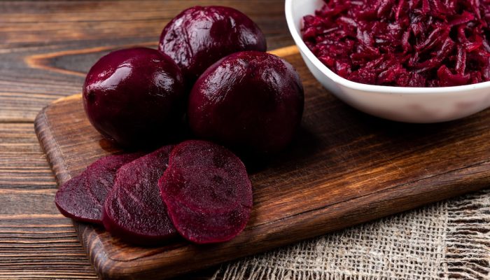 3 fatias de beterraba cozida a frente de três beterrabas cozidas inteiras, um prato com beterrab...