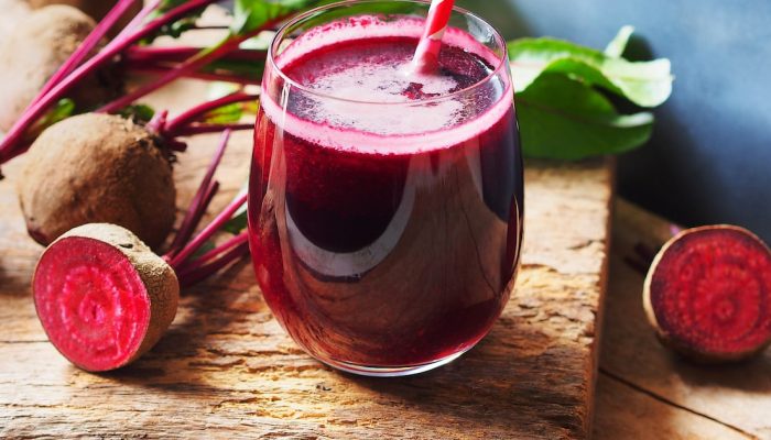 Suco de beterraba no copo de vidro com canudo com listras rosa, ao lado de várias beterrabas cor...